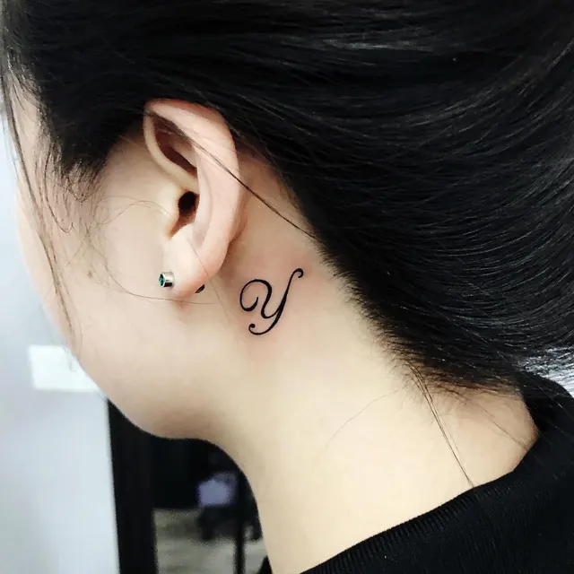 Fine-line initial letter tattoo behind the ear — WA Tattoo, Las Vegas